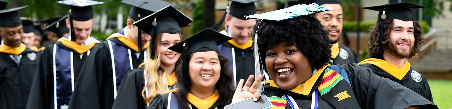 Black female graduate waves at photographer in procession
